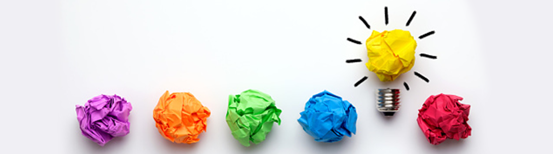 Colorful, balled up pieces of paper. The yellow ball of paper is higher than the other colors and looks and shines like a lightbulb.